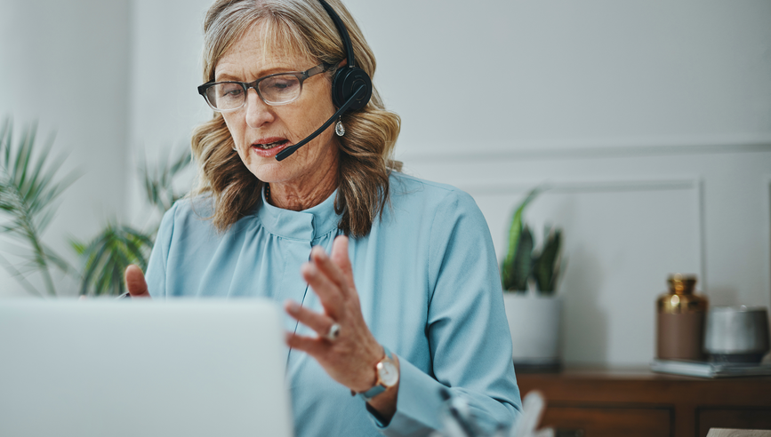 Shot of a mature woman using a headset and laptop in a modern office