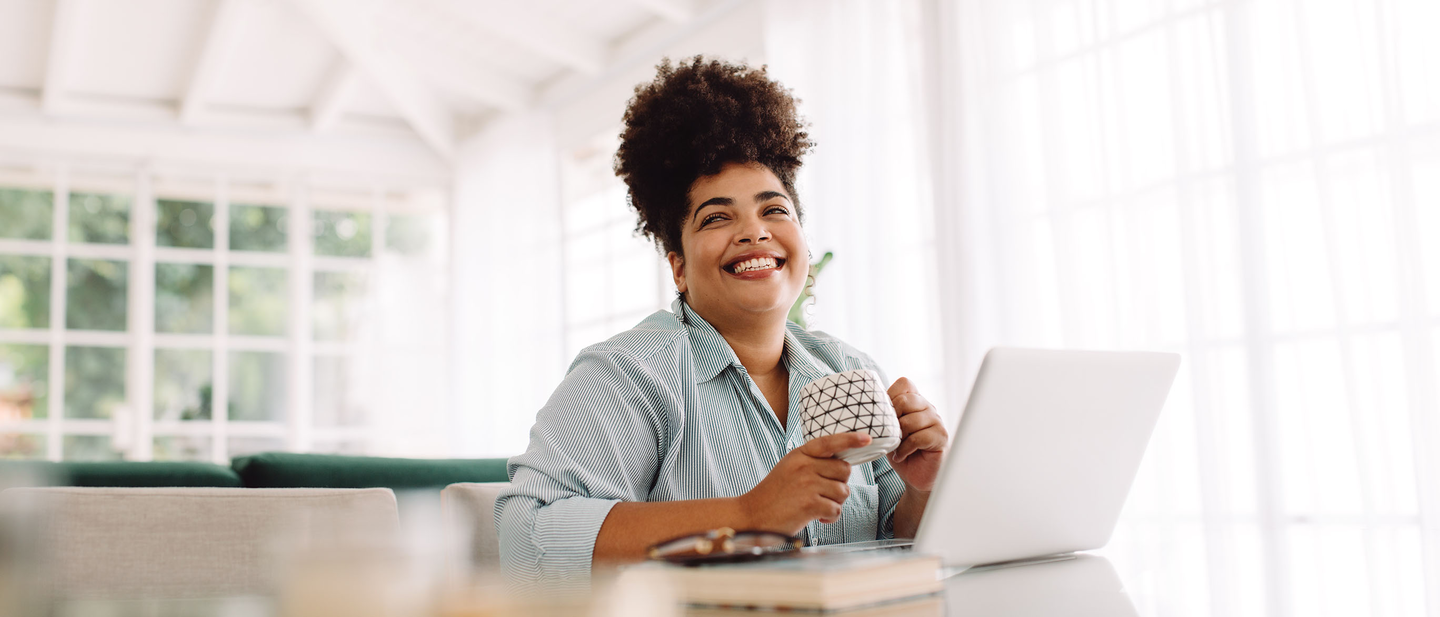 Woman smiles while at her computer in a light-filled room.