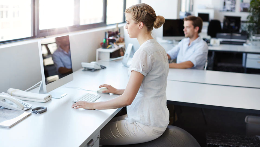 Woman sitting on exercise ball in modern office.