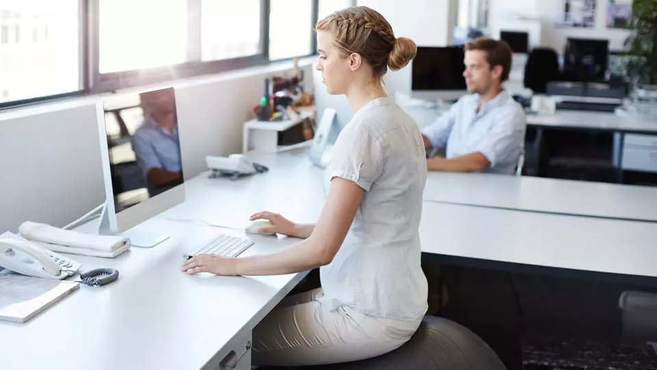 Woman sitting on exercise ball in modern office.