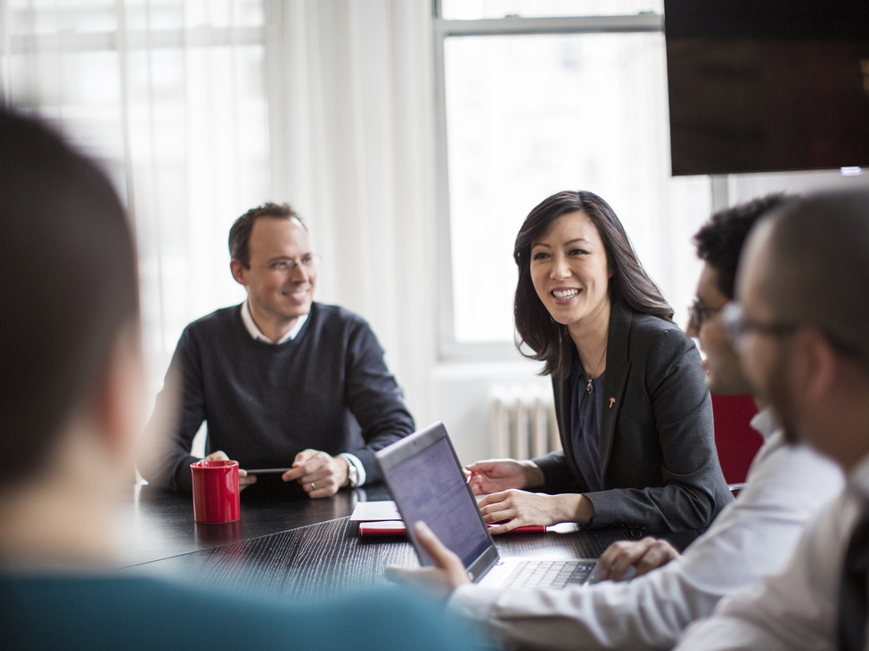 Smiling business professionals meet at a conference table.