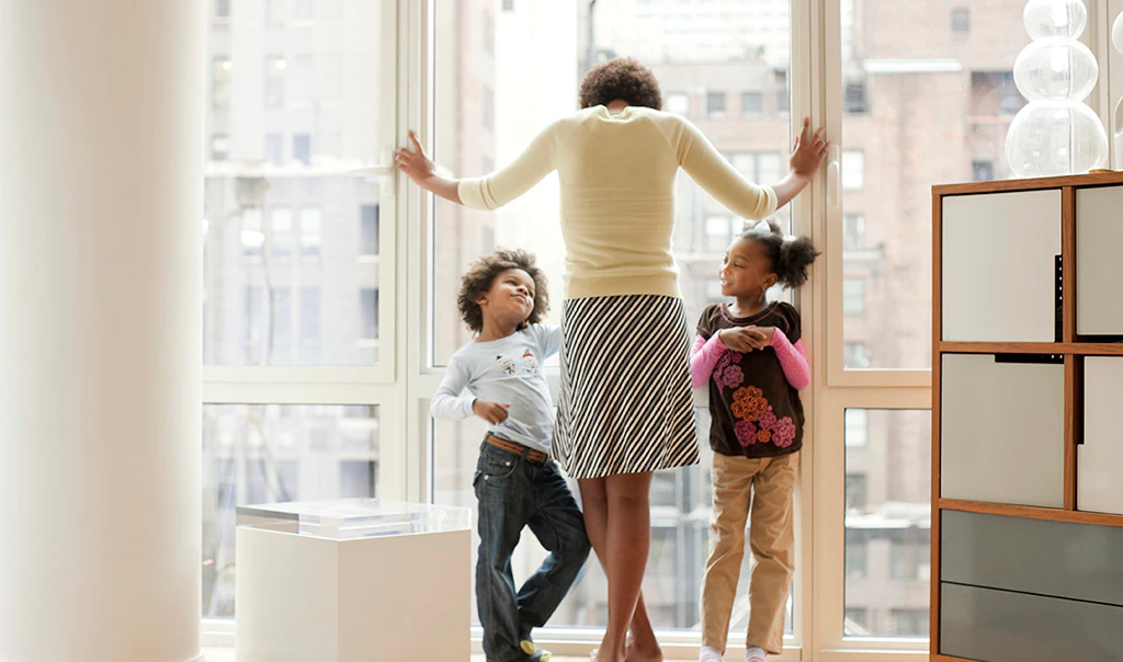 Woman standing with kids looking out window of condo.