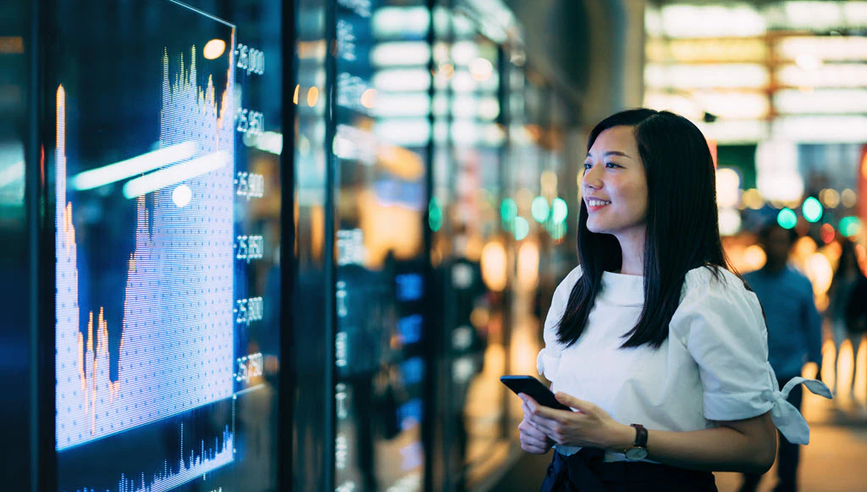 Woman starting at large screen with finance charts.