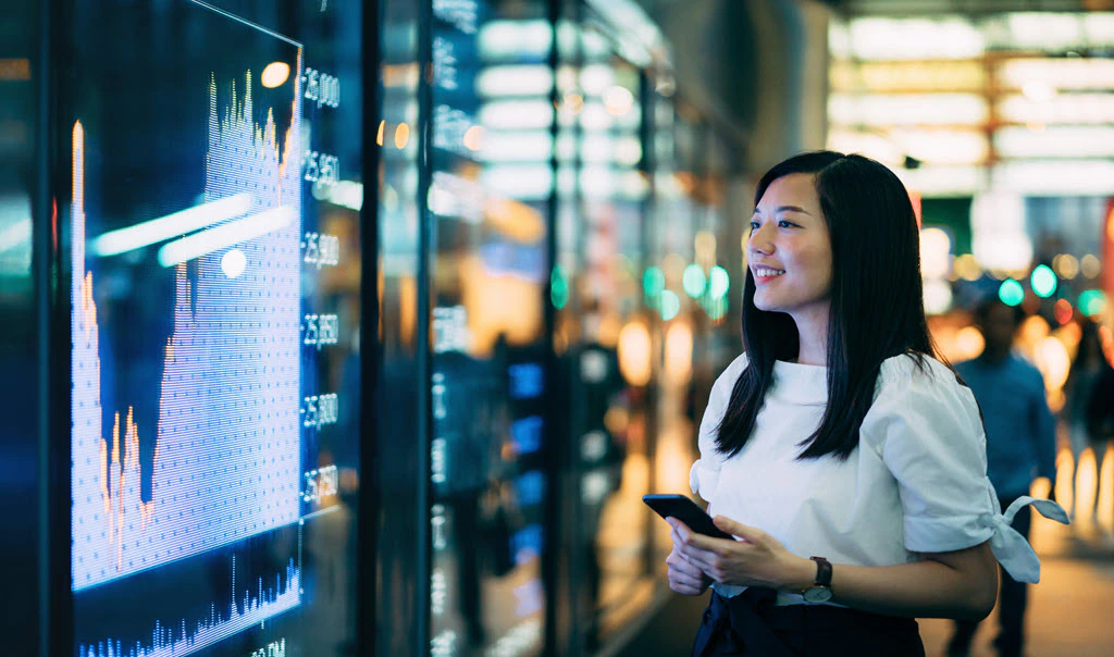 Woman starting at large screen with finance charts.