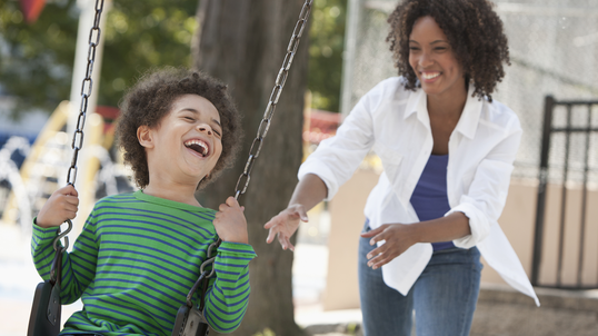 Mother pushing son on playset in their backyard.