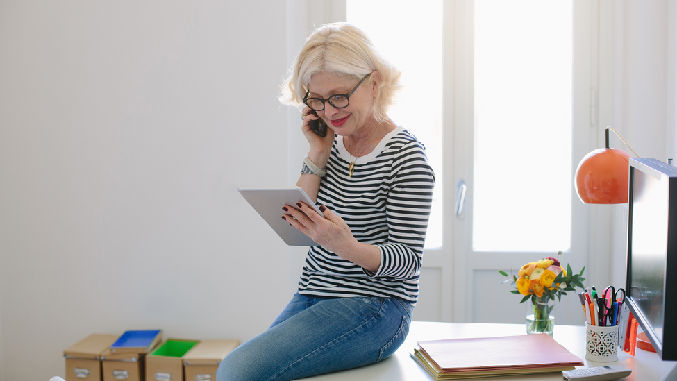 woman wearing striped shirt looking at tablet and talking on the phone