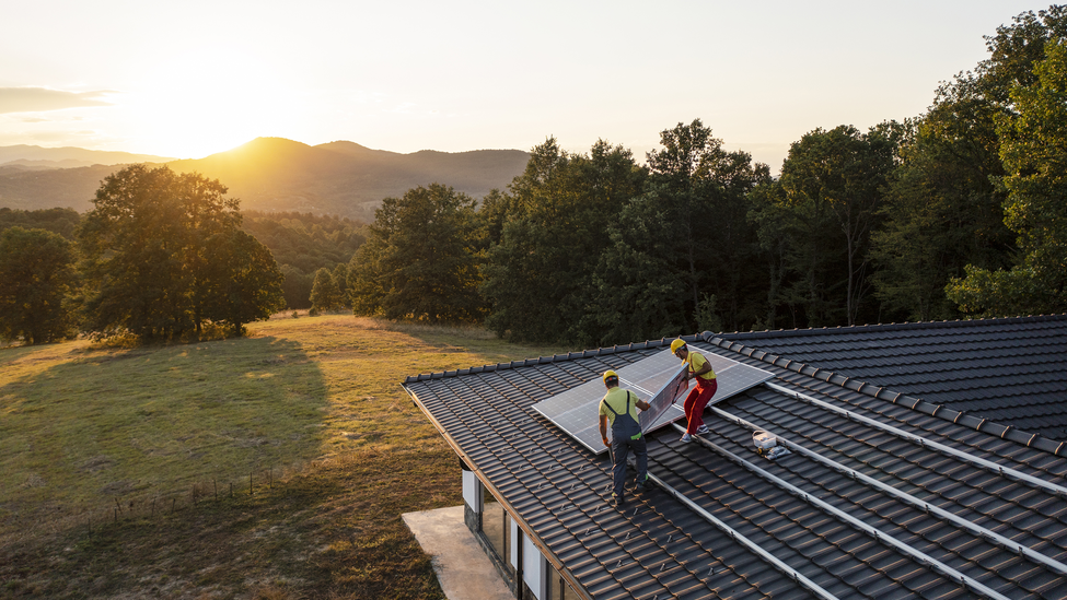 Professional workers installing solar panels on a roof at sunset.