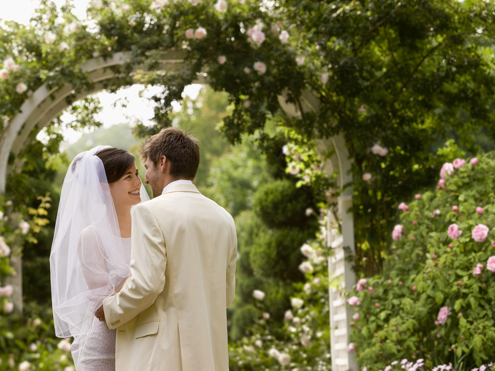 Partners prepare to kiss under a flower-filled trellis at their wedding.
