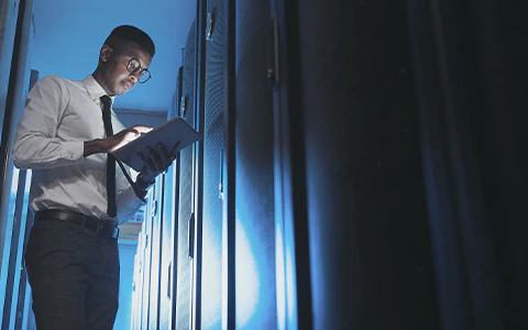 Young man looking down at tablet in server room.