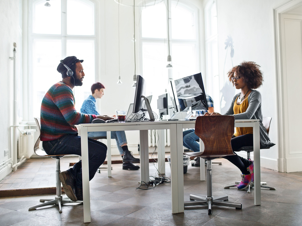 Small business workers sit at shared desk area while providing professional services virtually to clients.