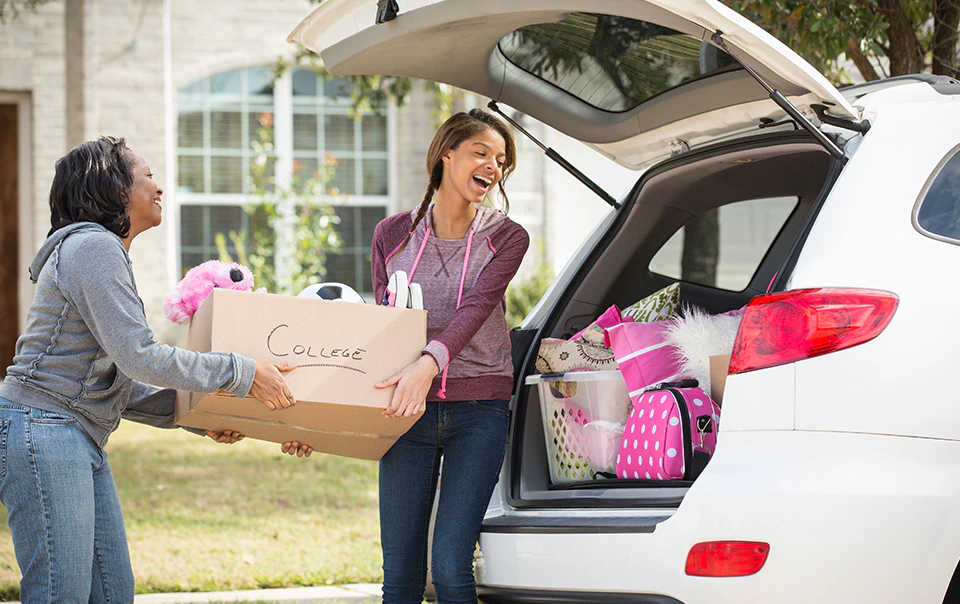 Young woman and her mom packing boxes into a car, heading off to college.
